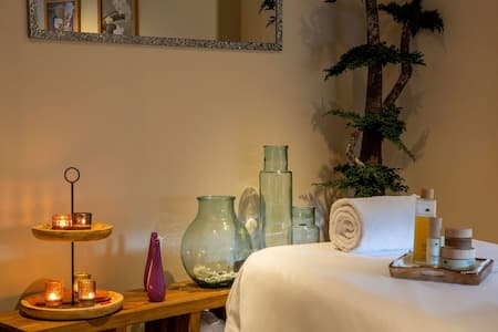 Massage table with towel, treatments, lit candles and plant, relaxing atmosphere and well-being.
