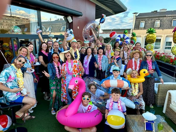 Summer party on the rooftop: smiling adults and children, tropical outfits, colorful buoys.